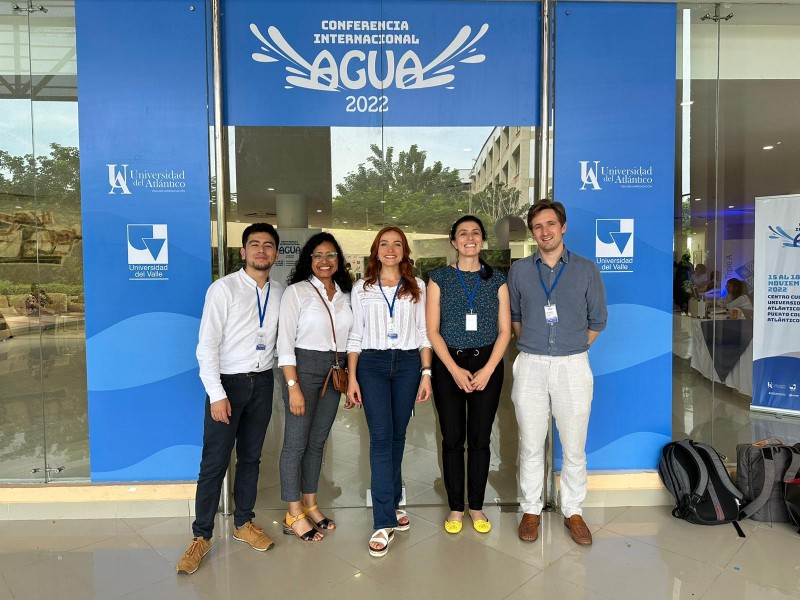 Five members of the team stand together smiling in front of the entrance to the AGUA Conference